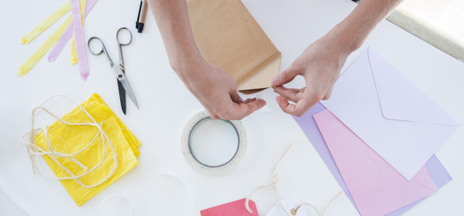 primer-plano-de-la-mano-de-la-mujer-envolviendo-la-caja-de-regalo-en-la-mesa